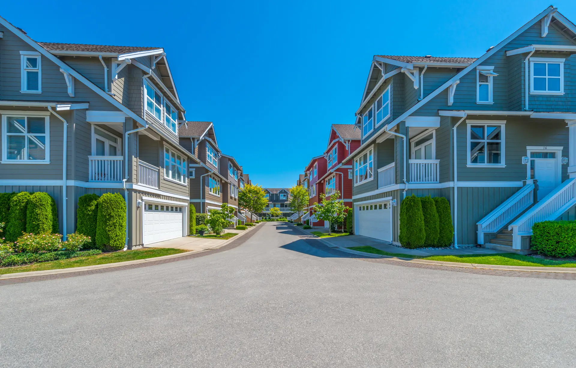 Suburban street with colorful, modern townhouses, blue sky, and neatly trimmed greenery.