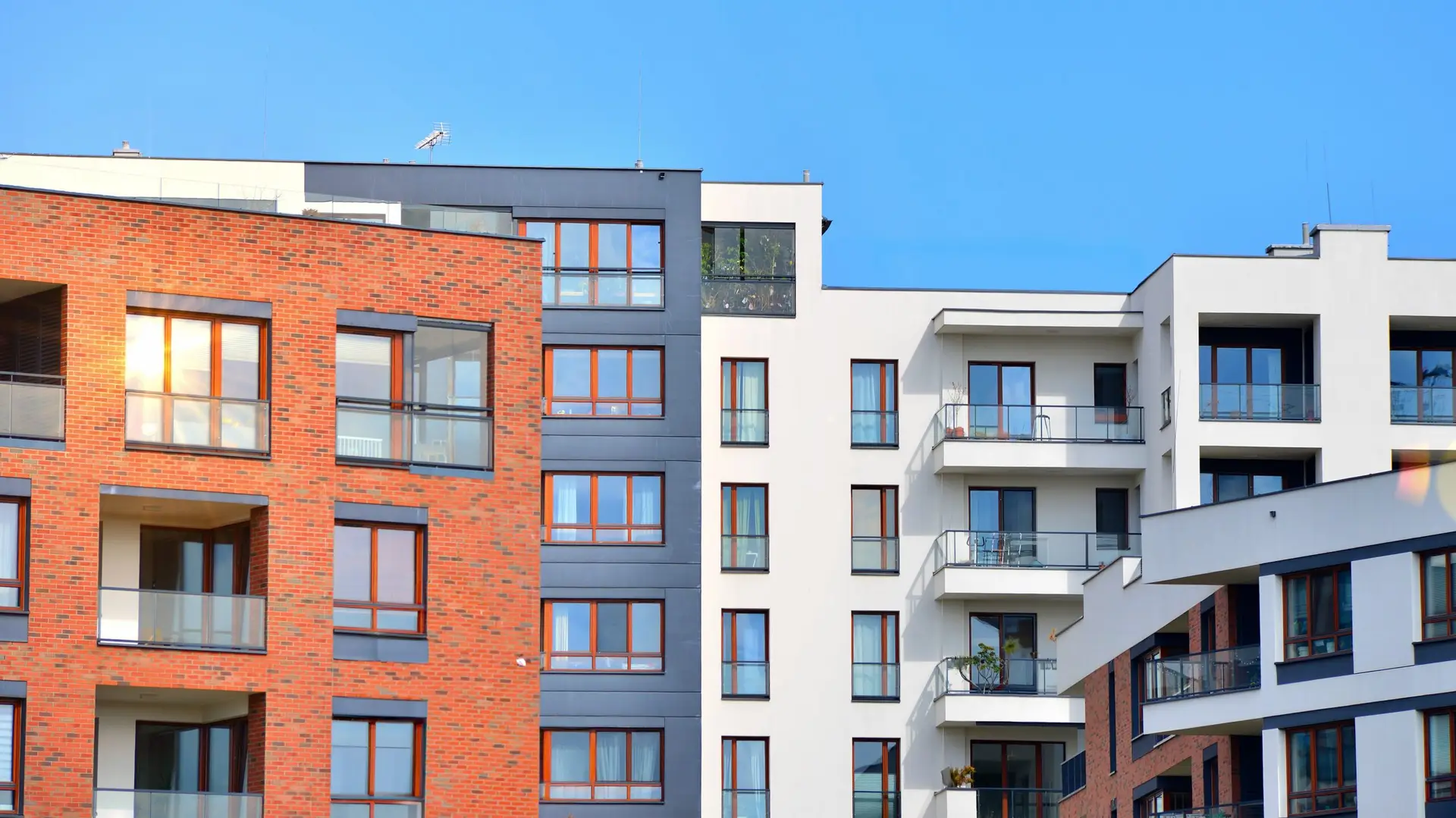 Modern apartment buildings with red brick and white facades under a clear blue sky.