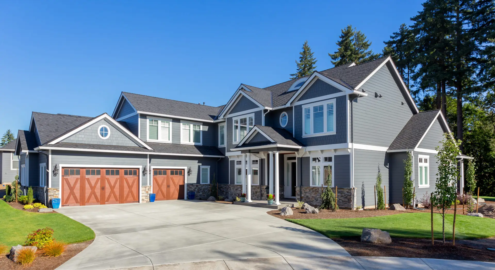 Modern two-story gray house with white trim, double garage, and landscaped yard under a clear blue sky.