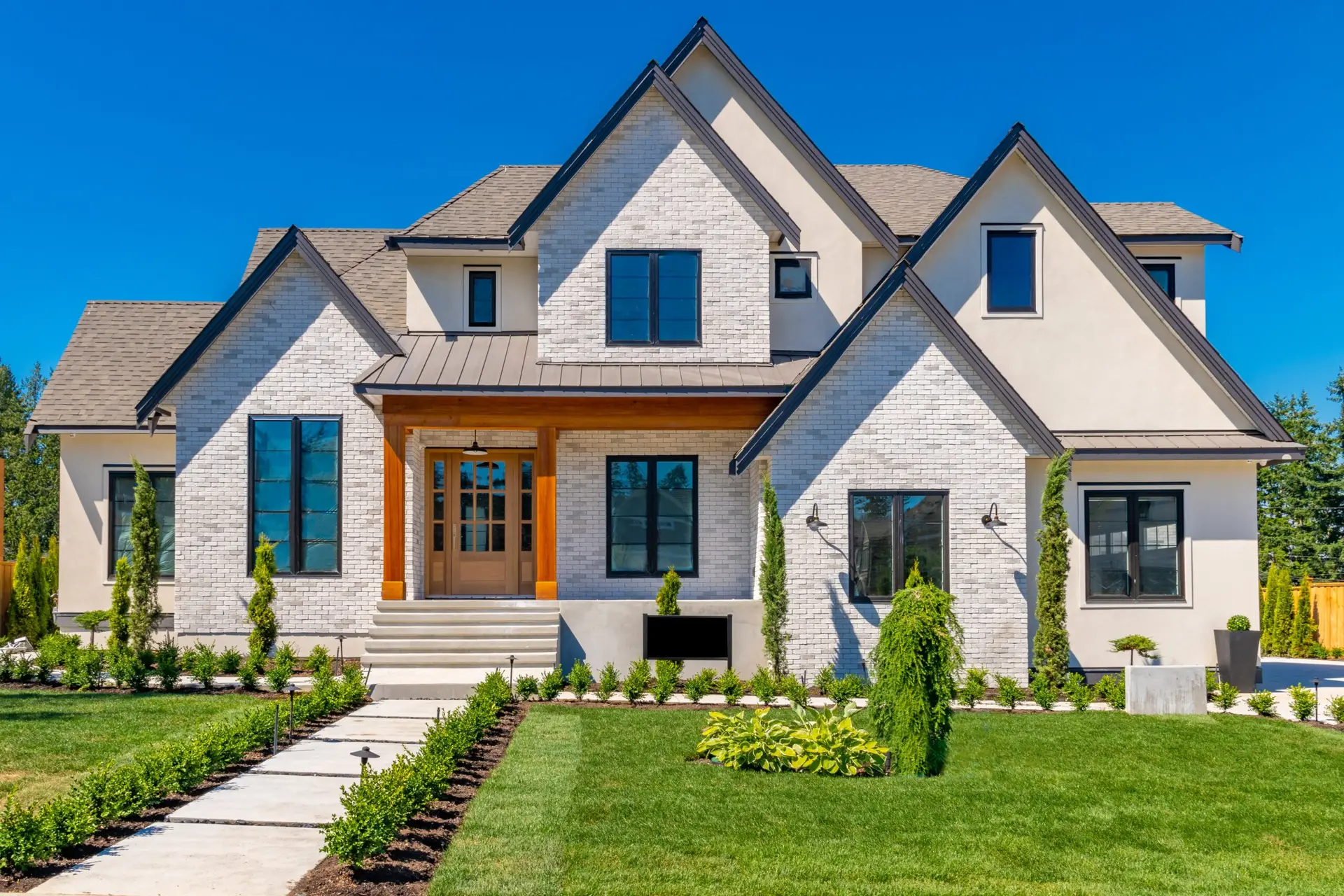 Modern two-story house with gabled roof, white brick facade, wooden front door, and landscaped garden.