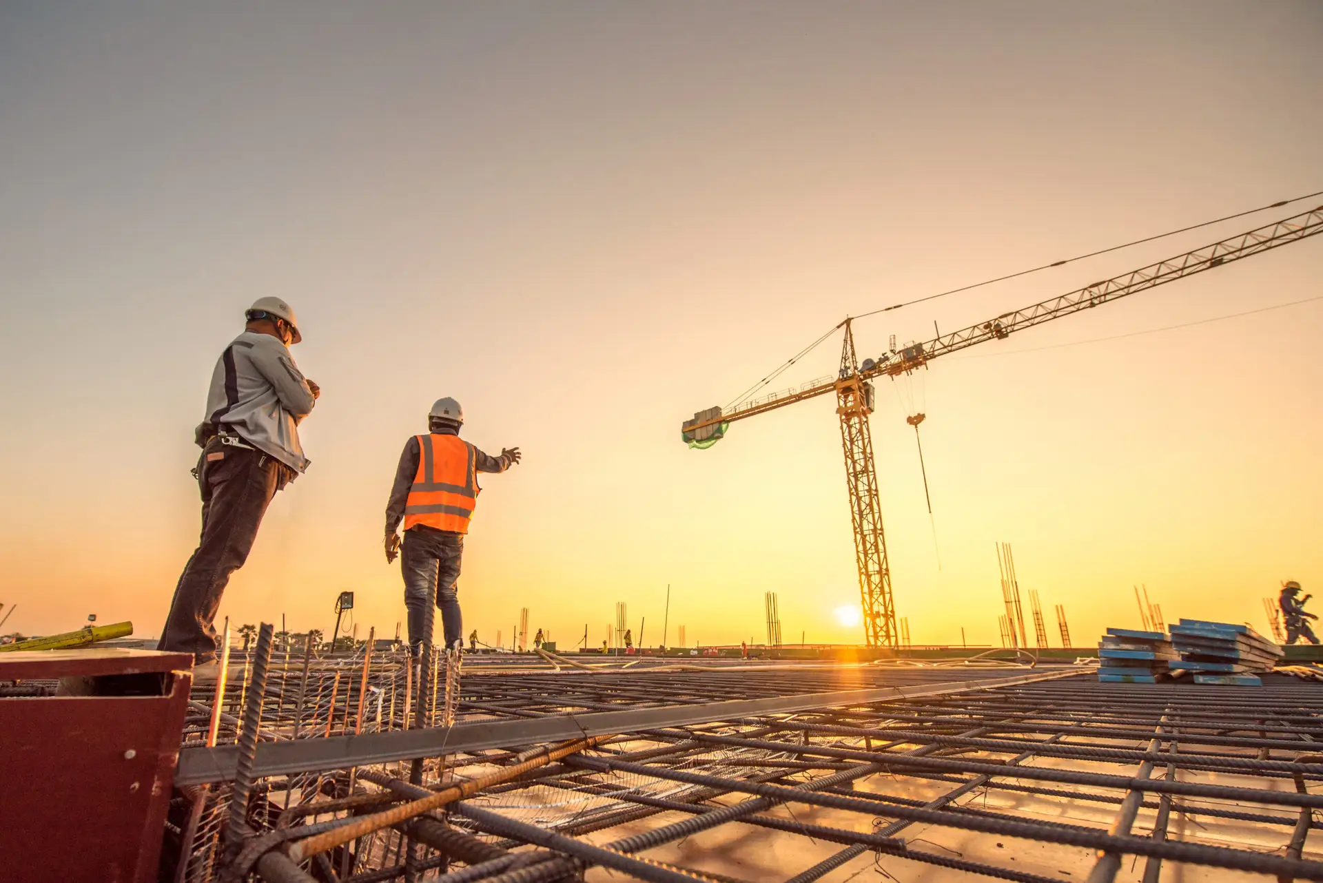 Construction workers on site at sunset with a crane in the background.